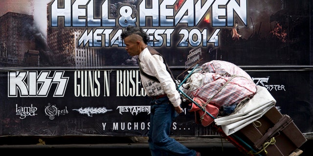 A man pulls a dolly loaded with supplies past publicity of "Hell and Heaven Metal Fest" concert, posted on bus in Mexico City, Friday March 7, 2014. The Mexico state government canceled the concert saying the March 15-16 "Hell and Heaven Metal Fest" planned for a fairground just east of Mexico City did not have adequate safety plans, posing a risk to concert-goers. (AP Photo/Eduardo Verdugo)