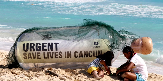 A giant message in a bottle from Oxfam International sits on the beach next to children playing in Cancun, Mexico, Sunday, Nov. 28, 2010. Facing another year without a global deal to curb climate change, the world's nations will spend the next two weeks in Cancun, Mexico, during the annual conference of the 193-nation U.N. climate treaty, debating how to mobilize money to to tackle a changing climate.