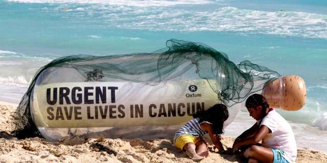 A giant message in a bottle from Oxfam International sits on the beach next to children playing in Cancun, Mexico, Sunday, Nov. 28, 2010. Facing another year without a global deal to curb climate change, the world's nations will spend the next two weeks in Cancun, Mexico, during the annual conference of the 193-nation U.N. climate treaty, debating how to mobilize money to to tackle a changing climate.
