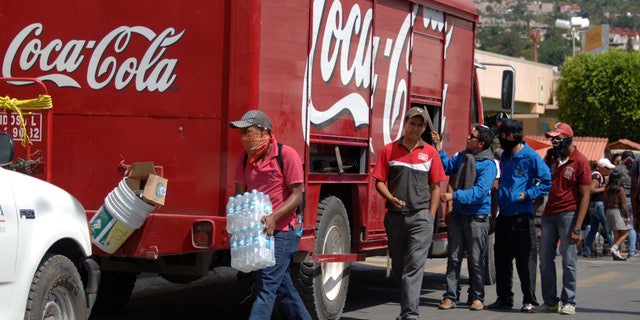 In this Nov. 4, 2014 photo, masked protesters begin to empty a Coca-Cola distribution truck in the city of Chilpancingo, Mexico. Coca-Cola Femsa SA, the brand's largest bottler in Mexico, has temporarily suspended operations in the capital of the embattled state of Guerrero following attacks on its workers and its trucks. The decision comes amid protests in the southern state around the disappearance of 43 students. Protesting students and teachers have regularly blockaded roads and taken over vehicles delivering everything from milk to snacks. (AP Photo/Alejandrino Gonzalez)