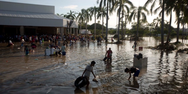 People wade through waist-high water in a store's parking, looking for valuables, south of Acapulco, in Punta Diamante, Mexico, Wednesday, Sept. 18, 2013. Mexico was hit by the one-two punch of twin storms over the weekend, and the storm that soaked Acapulco on Sunday - Manuel -re-formed into a tropical storm Wednesday, threatening to bring more flooding to the country's northern coast. With roads blocked by landslides, rockslides, floods and collapsed bridges, Acapulco was cut off from road transport. (AP Photo/Eduardo Verdugo)
