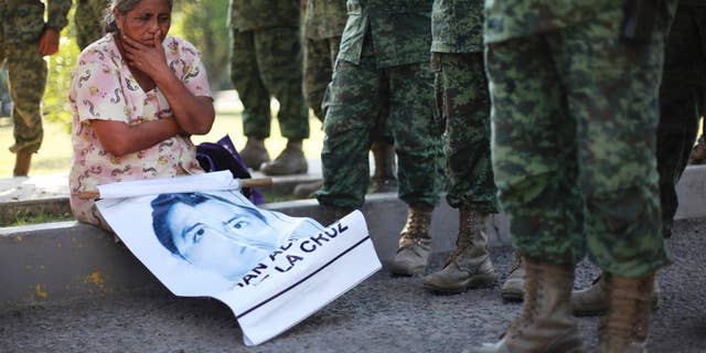 FILE - In this Dec. 18, 2014 file photo, the mother of missing college student Adan Abarajan de la Cruz sits at the foot of soldiers outside a military base during a protest by the families of 43 missing students over the army's alleged responsibility or lack of response to the students' disappearance in Iguala, Mexico. A group of independent experts said Monday, Aug. 17 2015, that Mexican authorities withheld information from family members of 43 college students who disappeared after a confrontation with police, not notifying them that some of the young men’s clothing was discovered shortly after they went missing. (AP Photo/Felix Marquez, File)