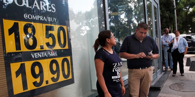 FILE - In this Sept. 19, 2016 file photo, people stand outside an exchange house advertising the sale of U.S. dollars at the rate of 19.90 Mexican pesos per dollar in Mexico City. U.S. election day cannot come soon enough for the Mexican peso, especially if Hillary Clinton is the winner. The currency has been pummeled in 2016, losing close to 10 percent of its value against the U.S. dollar, and briefly breaking the psychological barrier of 20 pesos per dollar. Its few bright spots have come after Clintons debate performances against Donald Trump. (Photo AP Photo/Marco Ugarte, File)