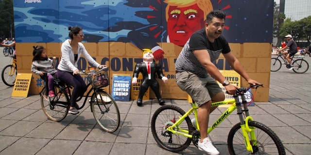 In this Sunday, Sept. 25, 2016 photo, a family of three ride their bicycles past a piÃ±ata depicting U.S. Republican presidential nominee Donald Trump propped against a cardboard mural wall with a message in Spanish that reads; "United against Trump" at the Angel of  Independence monument in Mexico City.  The head of Mexicoâs central bank told the Radio Formula network Friday, Sept. 30, 2016, that a Trump presidency âwould be a hurricane and a particularly intense one if he fulfills what he has been saying in his campaign.â  (AP Photo/Marco Ugarte)