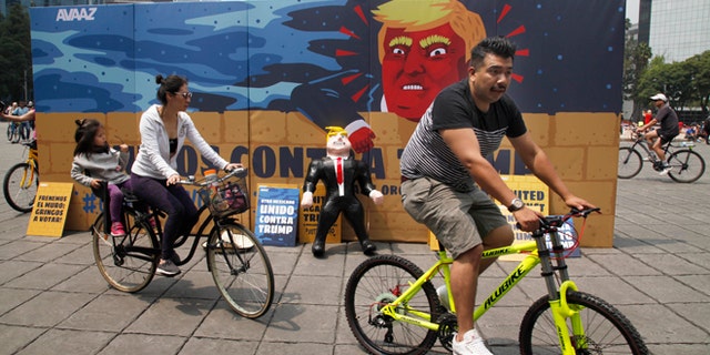 In this Sunday, Sept. 25, 2016 photo, a family of three ride their bicycles past a piñata depicting U.S. Republican presidential nominee Donald Trump propped against a cardboard mural wall with a message in Spanish that reads; "United against Trump" at the Angel of Independence monument in Mexico City. The head of Mexicoâs central bank told the Radio Formula network Friday, Sept. 30, 2016, that a Trump presidency âwould be a hurricane and a particularly intense one if he fulfills what he has been saying in his campaign.â (AP Photo/Marco Ugarte)