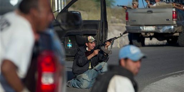 Member of a self-defense group barricade themselves against possible a possible ambush as they arrive to the village of Las Yeguas, Michoacan state, Mexico, Saturday, Jan. 11, 2014. Residents from various towns in Michoacan are protesting the arrival of vigilantes, or members of "self-defense" groups, to their communities. Vigilante groups have formed to confront drug cartels in parts of Michoacan. The Knights Templar ( Los Templarios ), a quasi-religious drug cartel, controls the area and most of the state.(AP Photo/Eduardo Verdugo)