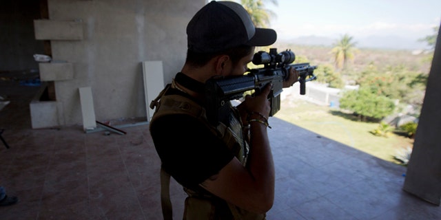 A man belonging to the Self-Defense Council of Michoacan, (CAM), peers through the sight of his weapon at a checkpoint in Nueva Italia, Mexico, Monday, Jan. 13, 2014. A day earlier the self-defenses encountered resistance as they tried to rid the town of the Knights Templar drug cartel while the government announced today that federal forces will take over security in a large swath of a western Mexico that has been hard hit by violence. (AP Photo/Eduardo Verdugo)