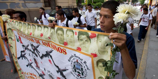 October 14, 2014: Students hold a banner with the faces of the missing that reads in Spanish 'cradle of murders'  during a march with flowers and candles to protest the disappearance of 43 students from the Isidro Burgos rural teachers college in Chilpancingo, Mexico. (AP Photo/Eduardo Verdugo)