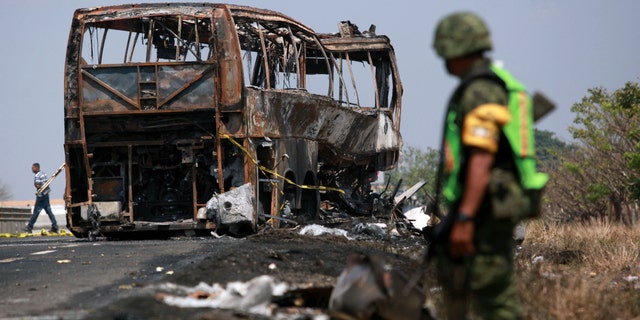 A soldier guards the site where a passenger bus slammed into a broken-down truck and burst into flames near the town of Ciudad Isla in the Gulf state of Veracruz, Mexico, Sunday, April 13, 2014. Dozens of people traveling on the bus to Mexico City burned to death inside the bus. (AP Photo/Felix Marquez)