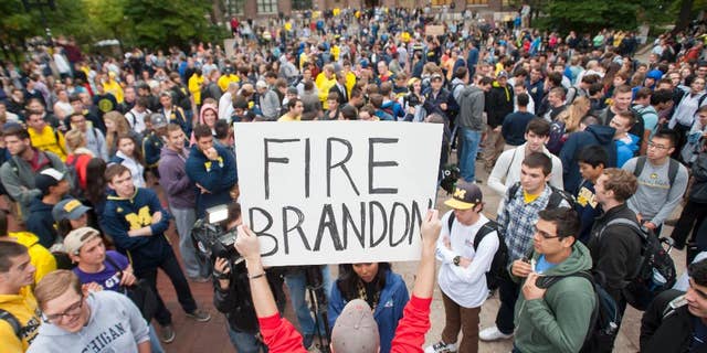 In a Sept. 30, 2014 photo, law student Edward Mears holds a "Fire Brandon" sign during a protest on the campus of the University of Michigan over the recent football game against Minnesota where quarterback Shane Morris was left in the game after receiving a concussion. About 1,000 University of Michigan students marched to the home of school President Mark Schlissel to protest against the performance of athletic director Dave Brandon and football coach Brady Hoke. (AP Photo/The Detroit News, David Guralnick)