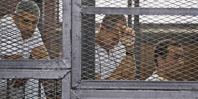 FILE - In this Thursday, May 15, 2014 file photo, from left, Mohammed Fahmy, Canadian-Egyptian acting bureau chief of Al-Jazeera, Australian correspondent Peter Greste, and Egyptian producer Baher Mohamed appear in a defendant's cage along with several other defendants during their trial on terror charges at a courtroom in Cairo. Egypt’s state news agency says the trial of three Al-Jazeera English journalists and 17 others has adjourned until next week when the judge will deliver the verdict, five months after the trial opened. Fahmy, Greste and Baher have been in detention since December 29. (AP Photo/Hamada Elrasam, File)