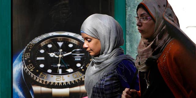 FILE - In this Monday, March 25, 2013 file photo, Egyptians walk in front of an advertisement for a watch in Cairo, Egypt. On midnight Thursday, Sept. 25, 2014, Egypt rolled back clocks one hour for the end of daylight savings time in the fourth time change in less than five months. Egypt is now two hours ahead of Greenwich Mean Time. In May the government moved clocks ahead one hour as a power-saving measure. It then switched clocks for the start and end of Ramadan, the Muslim fasting month, which this year fell in the scorching months of June and July. (AP Photo/Amr Nabil, File)