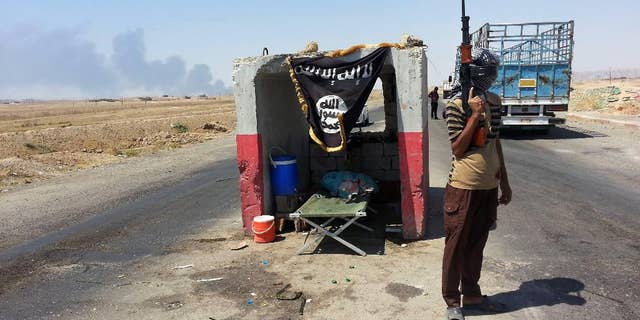 FILE - In this file photo taken Thursday, June 19, 2014, an al-Qaida-inspired militant stands guard at a checkpoint captured from the Iraqi Army outside Beiji refinery, some 250 kilometers (155 miles) north of Baghdad, Iraq. As Islamic militants rampaged across northern Iraq in June, seizing vast swaths of territory and driving hundreds of thousands of people from their homes, the Shiite Turkmens living in the hardscrabble town of Amirli decided to stay and fight. (AP Photo, File)