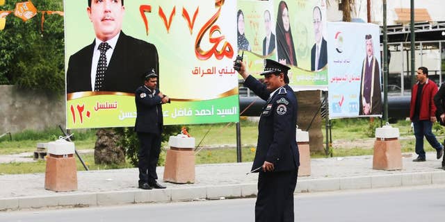 Iraqi traffic police officers control traffic in front of election campaign posters in Baghdad, Iraq,Tuesday April 1, 2014. The election campaign kicked off Tuesday with Iraqi towns and cities flooded with posters of the candidates for parliament seats on main streets and intersections. (AP Photo/Karim Kadim)