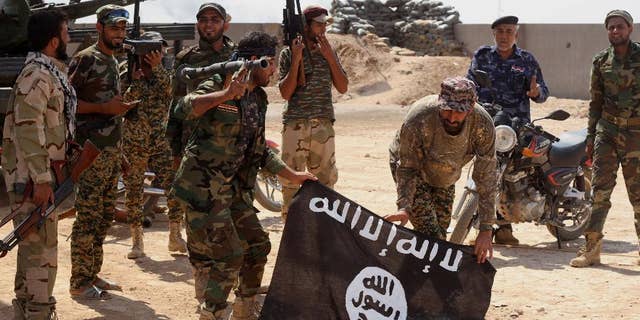 FILE - In this Tuesday, Oct . 7, 2014 file photo, Iraqi security forces hold a flag of the Islamic State group they captured during an operation outside Amirli, some 105 miles (170 kilometers) north of Baghdad, Iraq. The mass beheadings of Egyptian Christians by militants in Libya linked to the Islamic State group have thrown a spotlight on the threat the extremists pose beyond their heartland in Syria and Iraq, where they have established a self-declared proto-state. Militants in several countries have pledged allegiance to IS leader Abu Bakr al-Baghdadi. (AP Photo, File)