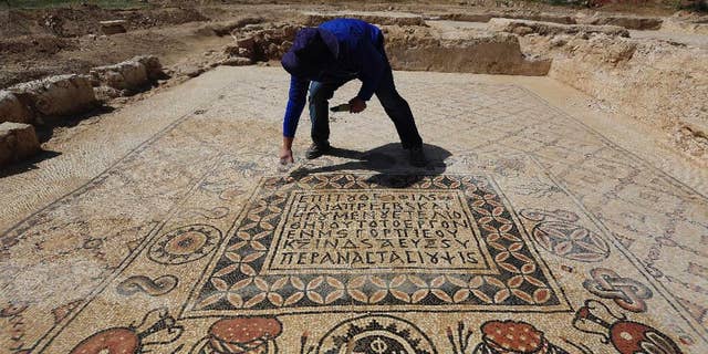 An Israeli Antiquities Authority archeologist Daniel Varge works on a Byzantine period monastery mosaic near a  village of Hura, Tuesday, April 1, 2014. Israel's Antiquities Authority has unveiled a monastery dating back about 1,400 years in the south of the country with an impressive mosaic floors that shed light on life in the region during the Byzantine period. (AP Photo/Tsafrir Abayov)