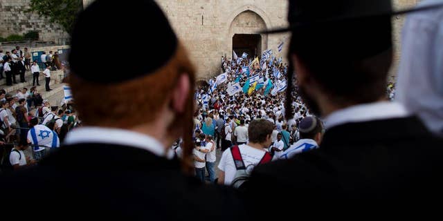 FILE - In this May 28, 2014, file photo, Ultra-Orthodox Jews watch people wave Israeli flags outside the Old City's Damascus Gate during Jerusalem Day celebrations in Jerusalem. A recent demonstration by ultra-Orthodox Jews against a new cinema opening its doors on the Sabbath was meant to be a show of strength in a long-running battle over the role of strict Jewish law in the cultural life of Jerusalem. But in many ways, it was also a sign of desperation after a series of gains by the city’s secular community in recent years.  (AP Photo/Dusan Vranic, File)