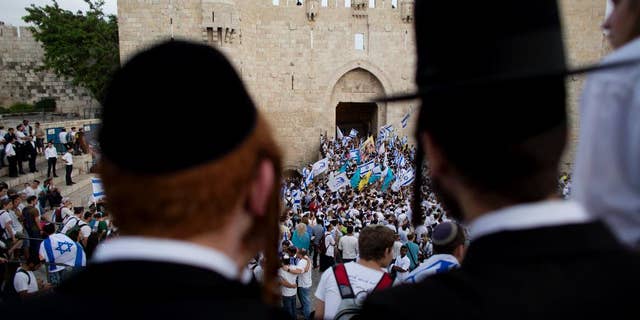 FILE - In this May 28, 2014, file photo, Ultra-Orthodox Jews watch people wave Israeli flags outside the Old City's Damascus Gate during Jerusalem Day celebrations in Jerusalem. A recent demonstration by ultra-Orthodox Jews against a new cinema opening its doors on the Sabbath was meant to be a show of strength in a long-running battle over the role of strict Jewish law in the cultural life of Jerusalem. But in many ways, it was also a sign of desperation after a series of gains by the city’s secular community in recent years. (AP Photo/Dusan Vranic, File)