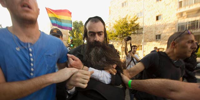 FILE - In this Thursday, July 30, 2015 file photo, ultra-Orthodox Jew Yishai Schlissel is detained by plain-clothes police officers after he stabbed people during a gay pride parade in Jerusalem. An Israeli hospital spokeswoman said Sunday, Aug. 2, that a teenage girl stabbed by Schlissel, an anti-gay extremist, in Thursday's attack during the parade has died. (AP Photo/Sebastian Scheiner, File)