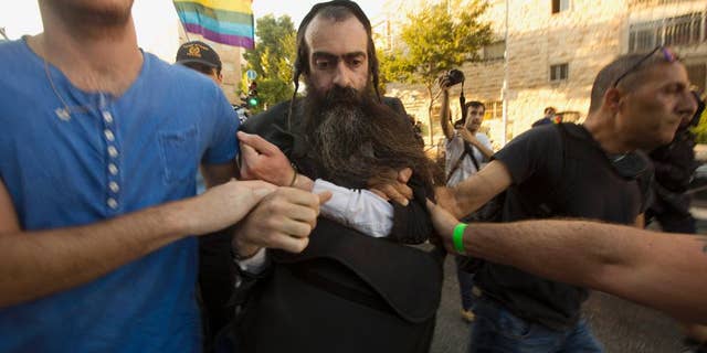 FILE - In this Thursday, July 30, 2015 file photo, ultra-Orthodox Jew Yishai Schlissel is detained by plain-clothes police officers after he stabbed people during a gay pride parade in Jerusalem. An Israeli hospital spokeswoman said Sunday, Aug. 2, that a teenage girl stabbed by Schlissel, an anti-gay extremist, in Thursday's attack during the parade has died. (AP Photo/Sebastian Scheiner, File)