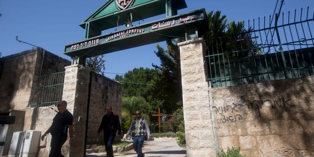 April 1, 2014: People walk past Hebrew graffiti that reads, "America equals Nazi Germany," at the Deir Rafat convent, central Israel.