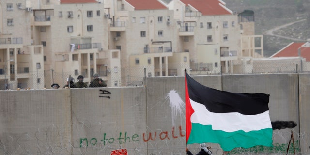 Feb. 17, 2012: In this file photo, the West Bank Jewish settlement of Modiin Illit is seen in the background while a protestor waves a Palestinian flag in front of Israeli troops during a protest against Israel's separation barrier in the West Bank village of Bilin.