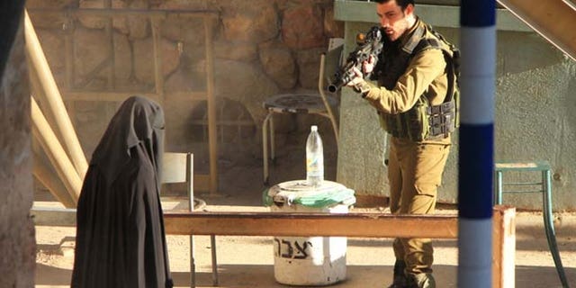 Sept. 22, 2015: An Israeli soldier aims at a Palestinian woman at a checkpoint in the West Bank city of Hebron.