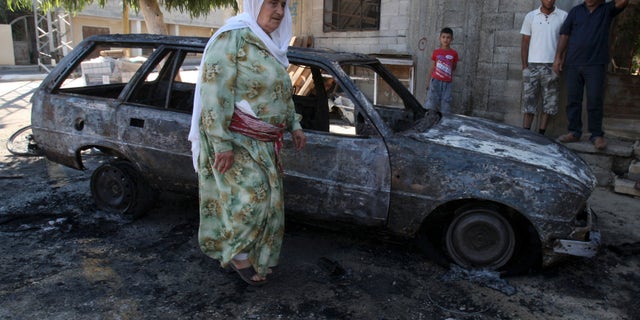 A Palestinian woman walks next to a burnt car in the village of Beit Furik, near the West Bank town of Nablus, Thursday, Sept. 15, 2011.