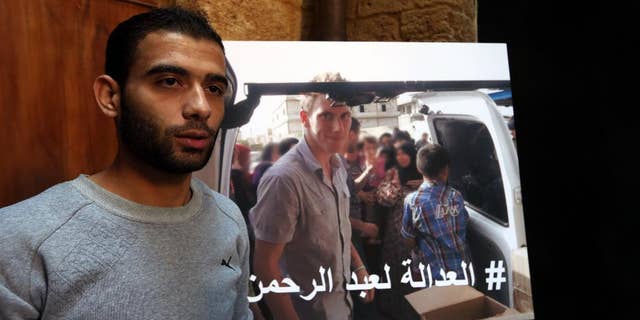 Syrian refugee Amjad Moghrabi stands in front of a photograph of his colleague, American aid worker Peter Kassig, 26, who converted to Islam while in captivity and changed his name to Abdul-Rahman Kassig, during an interview with The Associated Press in the northern port city of Tripoli, Lebanon, Saturday, Nov. 8, 2014. Kassig was helping victims of the Syrian civil war when he was captured in Syria last year and threatened with beheading by the Islamic State group. Arabic reads, "Justice for Abdul-Rahman." (AP Photo/Bilal Hussein)