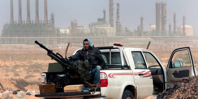 FILE - In this March 5, 2011 file photo, an anti-government rebel sits with an anti-aircraft weapon in front an oil refinery, after the capture of the oil town of Ras Lanouf, eastern Libya. The official Libyan news agency said Sunday, April 6, 2014 that the country's main militia in the east has agreed to hand back control of four oil terminals it captured and shut down last summer in its demand for a share in oil revenues. The shutdown has cost Libya millions of dollars. (AP Photo/Hussein Malla, File)