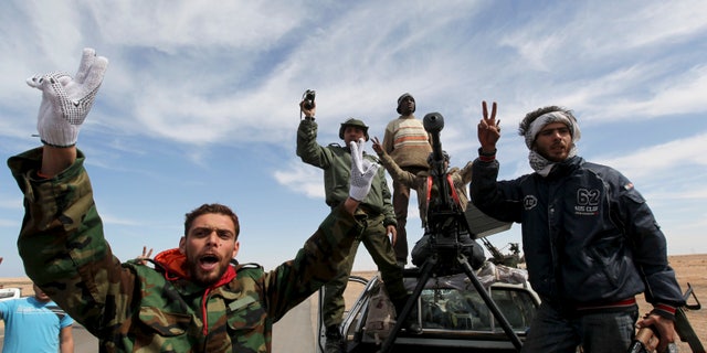 Anti-Libyan Leader Qaddafi rebels, stand on their vehicle react and flashe V sign at a desert road between Agela and Ras Lanouf towns, eastern Libya, on Saturday March 12, 2011. An emergency European Union summit on Libya brought a no-fly zone no closer, but leaders embraced a new Libyan opposition group as a viable partner after cutting all contact with strongman Qaddafi.
