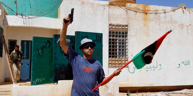 A Libya fighter celebrates as revolutionary fighters enter a Muammar Qaddafi political office next to a police station as they take control of Qaddafi loyalists villages in the desert some 730 km south of Tripoli, at Mahruga, 50 kms north of the southern city of Sebbah, Libya, Saturday, Sept. 17, 2011.