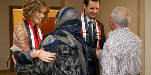 This photo taken on March 20, 2014, posted on the official Facebook page of the Syrian Presidency, shows first lady Asma Assad, left background, and Syrian President Bashar Assad, right background, shaking hands with Syrian teachers in Damascus, Syria.