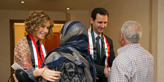 March 20, 2014: This photo posted on the official Facebook page of the Syrian Presidency, shows first lady Asma Assad, left background, and Syrian President Bashar Assad, right background, shaking hands with Syrian teachers in Damascus, Syria.
