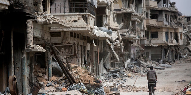 FILE - In this June 5, 2014, file photo, a man rides a bicycle through a devastated part of Homs, Syria. (AP Photo/Dusan Vranic, File)