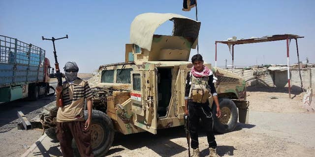 FILE - In this Thursday, June 19, 2014 file photo, Islamic State group militants stand with a captured Iraqi Army Humvee at a checkpoint outside Beiji refinery, some 250 kilometers (155 miles) north of Baghdad, Iraq. The Syrian foreign ministry said Tuesday, Sept. 23, 2014 that Washington informed Damascus' envoy to the United Nations before launching airstrikes against the Islamic State group in Syria, attacks that activists said inflicted casualties among jihadi fighters and civilians on the ground.(AP Photo)