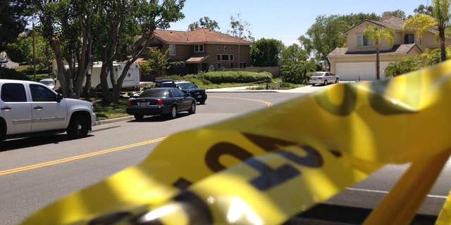 Police tape closes a street where four people were found dead in a home, center, on Tuesday, May 27, 2014 in suburban Mission Viejo, Calif. Authorities said the bodies were found by Orange County deputies making a welfare check after a relative's emergency call. The dead people were only described as two males and two females, and the Sheriff's Department was not releasing any information on how they may be related.(AP Photo/Gillian Flaccus)