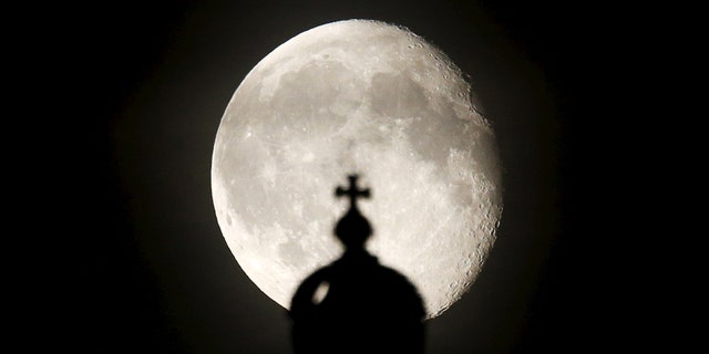 The moon rises next to a cross atop of the Reichstag building in Berlin, Germany, Aug. 2, 2015.