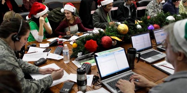 FILE - In this Dec. 24, 2012 file photo, Lizzie Solano, center, and her sister Sarah take phone calls from children asking where Santa is and when he will deliver presents to their house, during the annual NORAD Tracks Santa Operation, at the North American Aerospace Defense Command, or NORAD, at Peterson Air Force Base, in Colorado Springs, Colo. The U.S. and Canadian military will entertain millions of kids again this Christmas Eve with second-by-second updates on Santas global whereabouts. (AP Photo/Brennan Linsley, File)