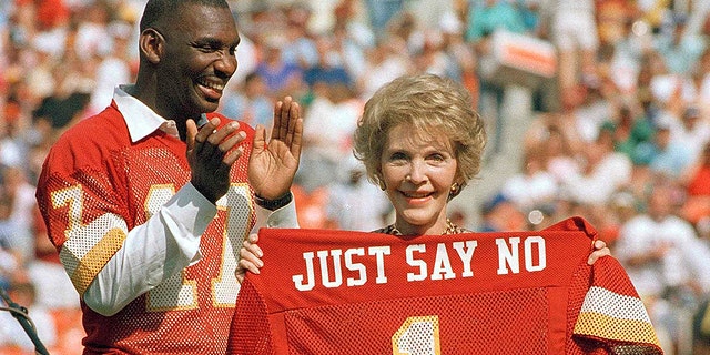 Washington Redskins quarterback Doug Williams stands behind First lady Nancy Reagan holding a jersey he gave her