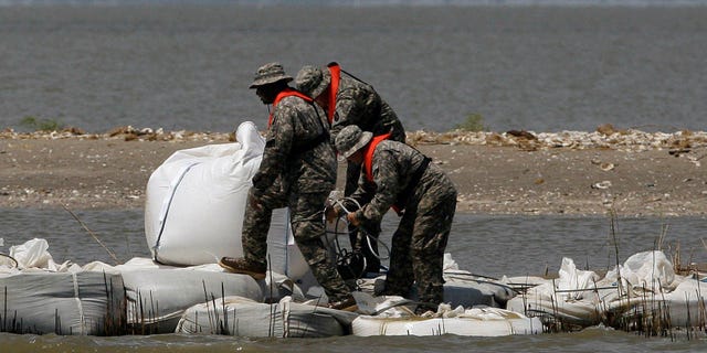 National Guardsmen walk along a barrier created by the National Guard from 2,000 pound bags of sand to block a pass in a effort to protect Scofield bay from oil from the Deepwater Horizon spill, Friday, June 11, 2010, near Venice, La.. (AP Photo/Eric Gay)