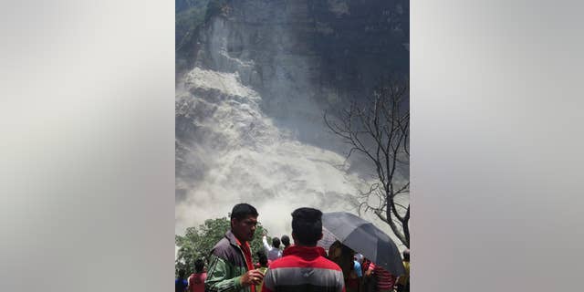 People gather at the site of a landslide north of Beni Bazaar, Nepal, Sunday, May 24, 2015. Thousands of people fled villages and towns along a mountain river in northwest Nepal on Sunday after it was blocked by a landslide that could burst and cause flash floods, officials said. (AP Photo/M.B. Astha)