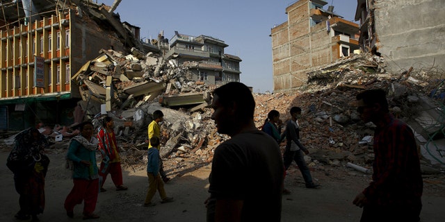 Nepalese people walk along a street near the debris of collapsed houses, a month after the April 25 earthquake in Kathmandu, Nepal May 25, 2015.