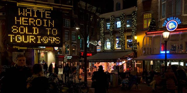 FILE - In this Dec. 5, 2014 file photo an electronic sign outside Amsterdam's famous Bulldog coffee shop, right, warns tourists of "white heroin", an extremely dangerous drug which is being sold as cocaine to tourists in Amsterdam. Police in Amsterdam said Tuesday April 7, 2015, that a 42-year-old man who turned himself in on Saturday could be a dealer who sold white heroin to tourists, telling them that it was cocaine, three tourists have died in recent months and 20 other became unwell after taking heroin. (AP Photo/Peter Dejong, File)
