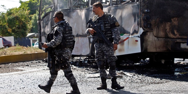 FILE - In this May 1, 2015 file photo, state police stand next to a charred passenger bus, that was extinguished by firefighters in Guadalajara, Mexico. Authorities in western Mexico asked residents to stay at home as they scrambled to extinguish burning vehicles that blocked roads in various parts of Guadalajara. Such blockades are a common cartel response to the arrest of important members or are used to foil police and military operations. (AP Photo, File)