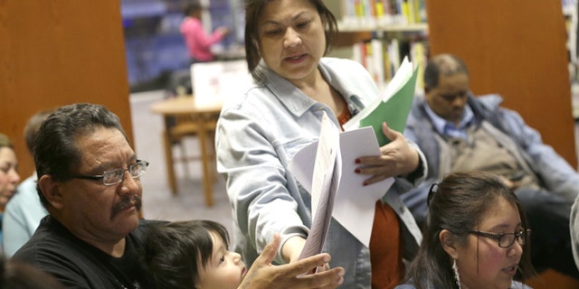 In this photo made Thursday, Feb. 12, 2015, JPS Health Network patient navigator Delaila Hernandez, center, helps Fred Cardenas with documents during a Affordable Care Act enrollment event at the Fort Worth Public Library in Fort Worth, Texas. Enrollment drives are being held across the country to help people beat the deadline to sign up for health insurance through the federal marketplace. But in Texas and more than two dozen other states where millions of people fall into a so-called coverage gap, the outreach effort has involved more than just signups. (AP Photo/LM Otero)