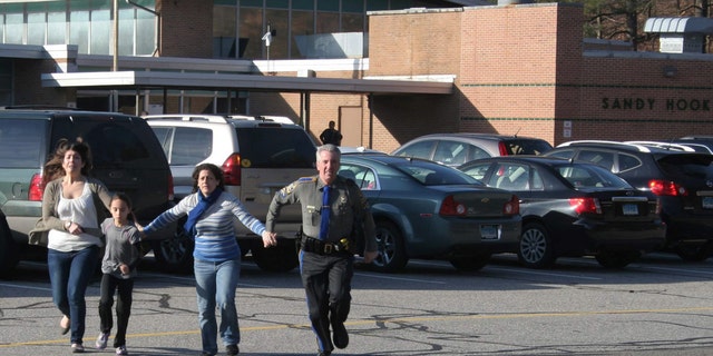 FILE - In this Friday, Dec. 14, 2012, file photo provided by the Newtown Bee, a police officer leads two women and a child from Sandy Hook Elementary School in Newtown, Conn., where a gunman opened fire, killing 26 people, including 20 children. A prosecutor is planning to release a report on the investigation into the massacre at Sandy Hook Elementary School on Monday, Nov. 25, 2013, but the public will have to wait longer for the Connecticut state policeâs full accounting of the crime.(AP Photo/Newtown Bee, Shannon Hicks, File) MANDATORY CREDIT: NEWTOWN BEE, SHANNON HICKS