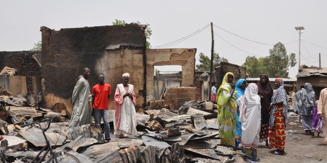 May 11, 2014 - People stand outside burnt houses following an attack by Islamic militants in Gambaru, Nigeria. Many brutalized residents of the once bustling town of Gamboru say they are moving across the border to Cameroon because they cannot trust the Nigerian government to protect them.