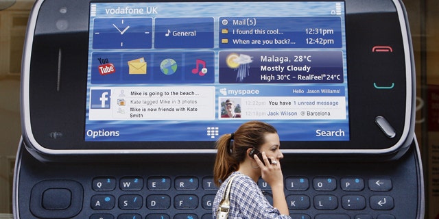 A woman uses her mobile telephone as she passes a Nokia advert in London.