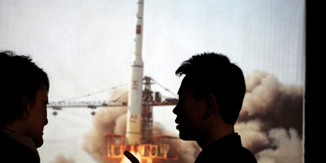 April 10, 2012: In this photo North Korean guide Kim Won Ho, right, speaks to a foreign journalist near a photo depicting the 2009 satellite rocket launch at the Three Revolutions exhibition hall in Pyongyang, North Korea.